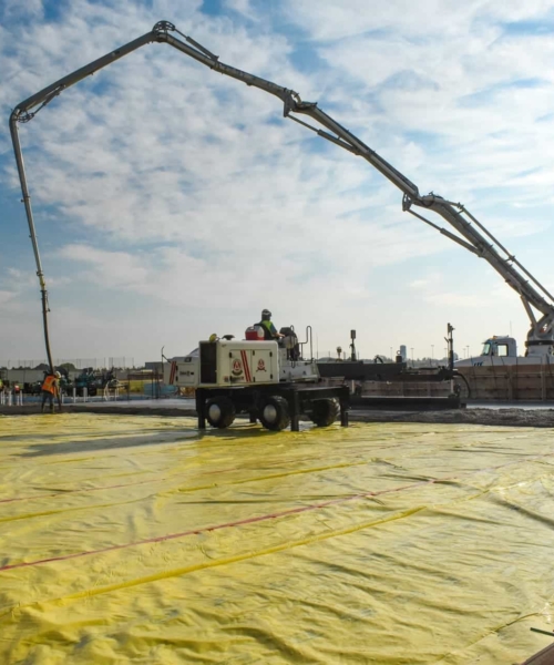 A laser screed working on leveling freshly poured concrete with a concrete pump in the background.
