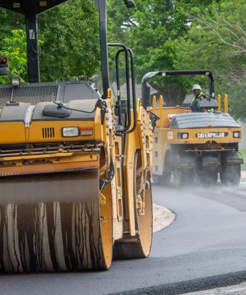 Asphalt rolling machines driving down a freshly poured residential asphalt road.